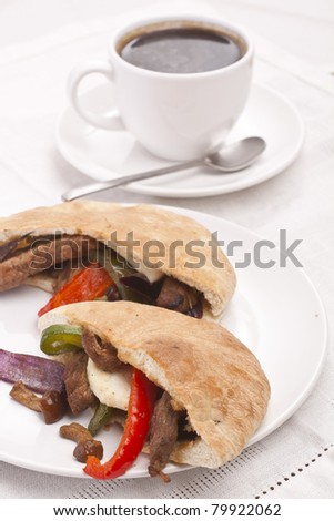 cup of black coffee and plate with halves of pita bread sandwiches with meat and vegetables