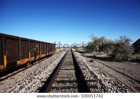 Railroad Tracks. View of empty railroad tracks  leading off into the horizon & framed by an empty coal tender & manzanita trees.