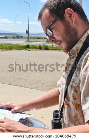 Lost in the Southwestern US. Man in beard & glasses studies map by roadside with desolate background.