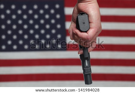 Gun Control USA Style/Hand holding automatic pistol over slightly blurred background of US Flag