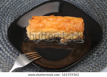 Bougatsa/Greek phyllo pastry filled with custard & covered with honey syrup on black plate with fork