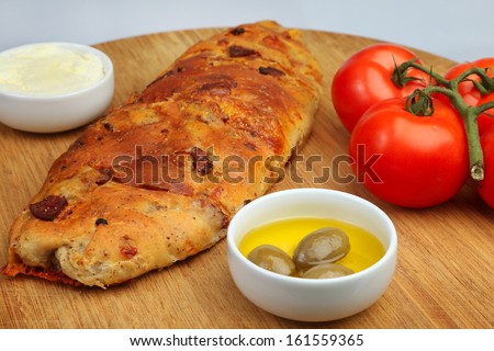 Pancetta bread on cutting board with small ceramic dishes of olive oil, butter & vine tomatoes to one side