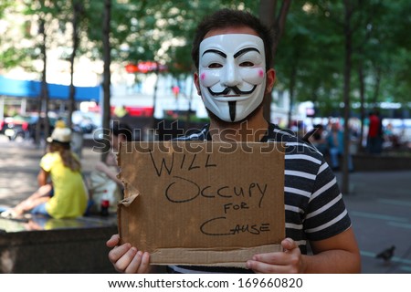 New York City - July 30 2012: Man Wearing Guy Fawkes Mask In Zuccotti Park Holding &Quot;Will Occupy For Cause&Quot; On Cardboard Sign With Parkgoers In Background