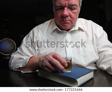 Middle age man staring down, clutching shot glass set upon Big Book of Alcoholics Anonymous with black background