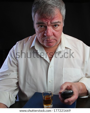 Middle age man clutching cordless phone with shot glass set upon Big Book of Alcoholic Anonymous with black background