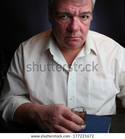 Middle age man clutching shot glass set atop Big Book of Alcoholics Anonymous with dark background