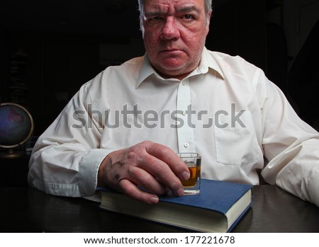 Middle age man staring straight ahead, clutching shot glass set upon Big Book of Alcoholics Anonymous with black background