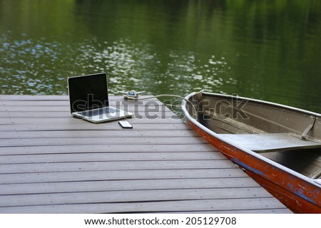 Smart phone & laptop computer on wood dock with aluminum rowboat & lake water in the background
