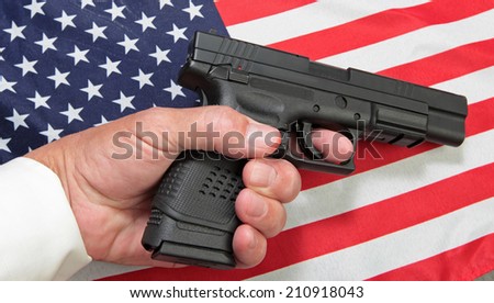 Limp man\'s hand holding automatic pistol against US flag.