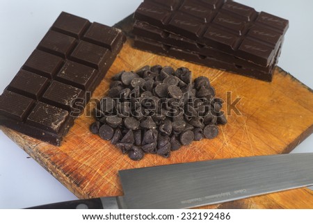 Baking chocolate in bars & drops arrayed on wood cutting board with chef knife