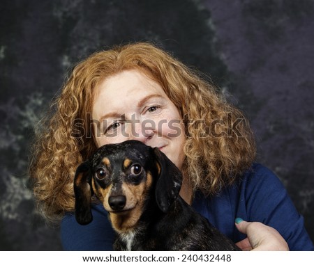 Red-haired woman with small black & brindle dog smiling against portrait background