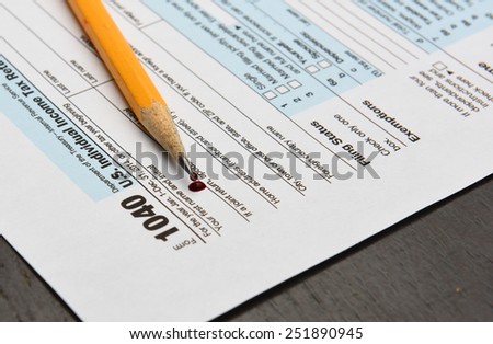 Internal Revenue Service form 1040 with sharpened pencil & drop of blood laid atop left-hand corner