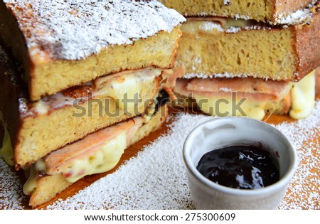 Monte cristo sandwich on wood platter with cheese, powdered sugar and pot of preserves