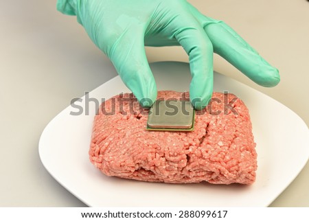 High tech foods series/surgically gloved hand place microprocessor into raw ground beef on white platter