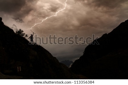 Dark image of lightning striking the staff of a silhouette person in the mountains