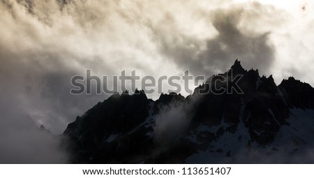 Backlit spiked mountain range with clouds around it