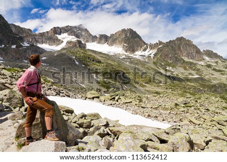 Young explorer in traditional clothing looks at the mountains in the Swiss Alps on a sunny summer day