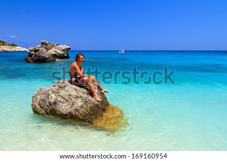 Handsome young man sits on a rock in the sea in summer on the greek island Zakynthos