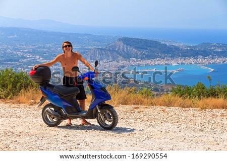 Young man enjoys the view over Zakynthos from his rented scooter in summer