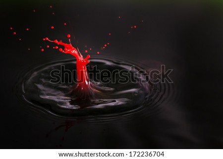 Beautiful image of a drop of red cream falling into dark water in the shape of a little man getting shot