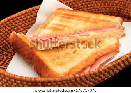 Grilled ham and cheese sandwich in a basket on a black background
