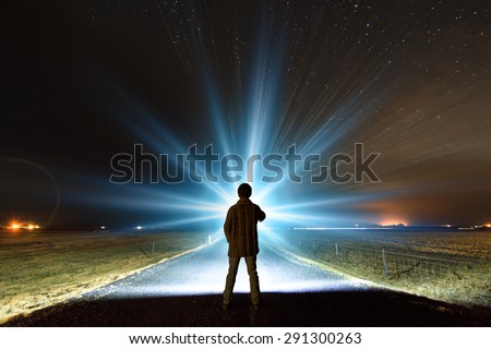 Young man shining a powerful torch on a starry night in Iceland, looking for the northern lights or aliens