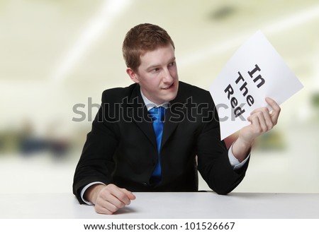 man in a suit sat at a desk look at a  piece of paper with the words in the red printed on it