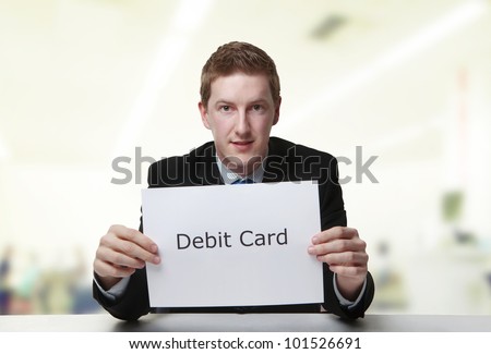 man in a suit sat at a desk look at a  piece of paper with the words debit card printed on it
