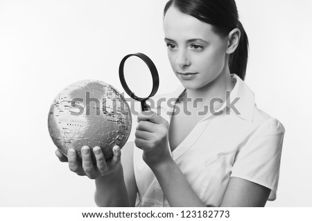 woman holding up a jigsaw globe puzzle and looking at it with a inspecting eye with a magnifying glass