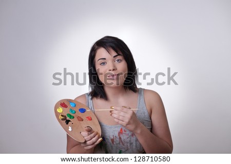 woman holding a artists painting palette and brush doing her make up