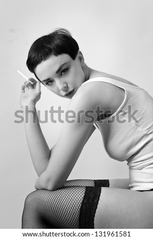sexy woman wearing a vest top siting down on a chair wearing fishnet hold ups smoking a cigarette