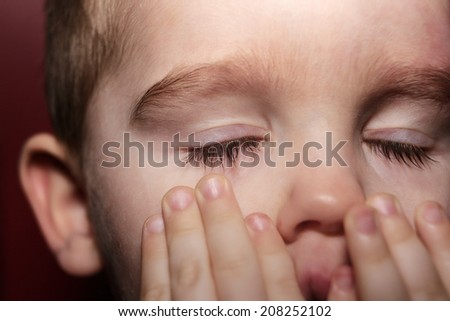 closer up shot of a young boys face not looking happy pulling his eye lid down