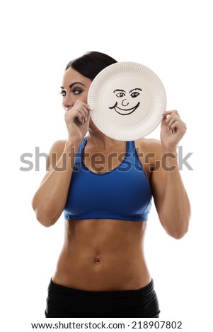 woman wearing sport bra and shorts holding a paper plate with a happy face draw on the plate over her face
