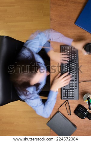 woman typing and working hard at her desk taken from a birds eye view with a long exposure so her movement is a blur