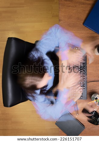 woman typing and working hard at her desk taken from a birds eye view with a long exposure and multiple exposures so all movement is a blur
