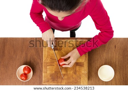 woman chopping up tomatoes on a wooden chopping board taken from a birds eye view from above