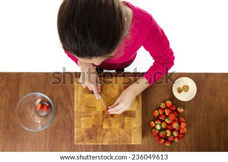 woman chopping up strawberries on a wooden chopping board taken from a birds eye view from above looking down