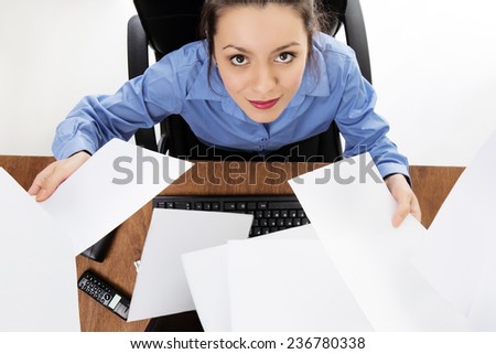 Woman sitting at her desk at work throwing paper up in the air. Image is shot from a birds eye view looking down.