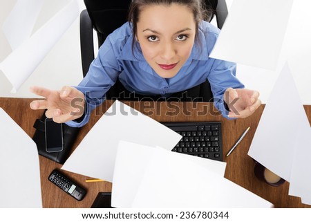 Woman sitting at her desk at work throwing paper up in the air. Image is shot from a birds eye view looking down.