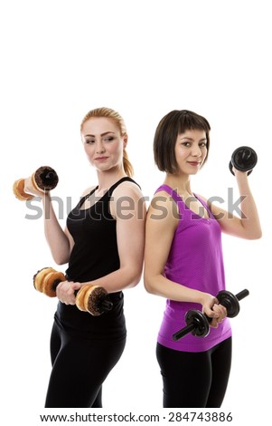 two fitness model standing back to back both are weight training with dumbbells but one instead of real weighs is using doughnuts.