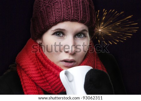 woman looking cold in winter clothes drinking a hot drink to keep warm with fireworks going off in the background