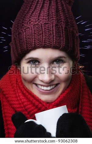 woman looking cold in winter clothes drinking a hot drink to keep warm with fireworks going off in the background