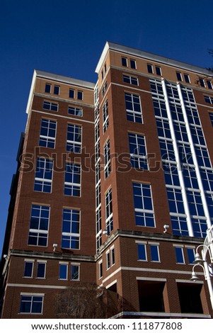 Tall brick building with blue tinted windows covered on two sides with clear blue sky