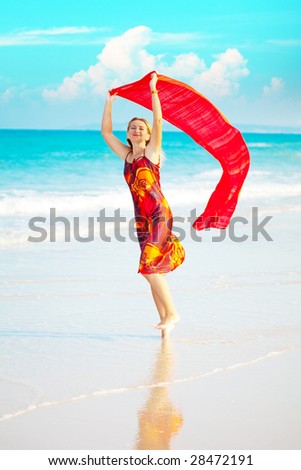 Beautiful woman walking near the ocean with red sarong