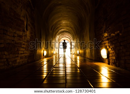 silhouette of human in old brick tunnel light at end of tunnel