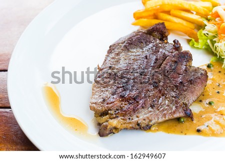 beef steak on white dish with salad french fries and pepper gravy sauce on wood table