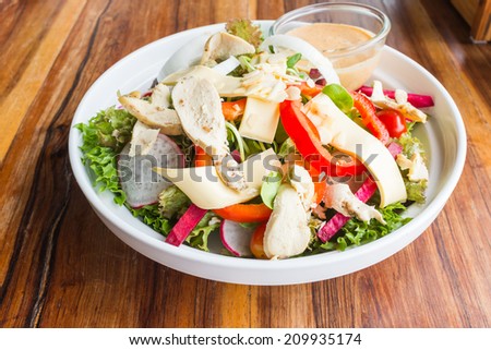 chicken cheese and vegetables salad with caesar dressing sauce in white dish on wood table in restaurant