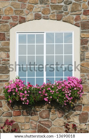 Window with flower box filled with pink petunia flowers on a rock wall.