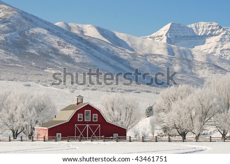 Large red barn in winter snow with tall mountains in the background.