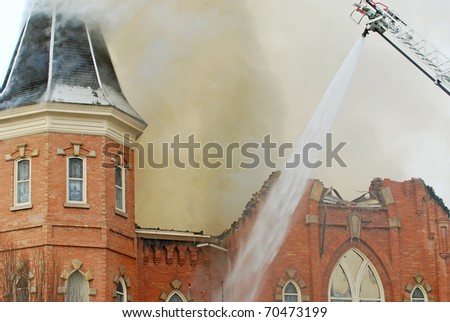 Church building on fire with firefighters spraying water on the walls from a ladder.
